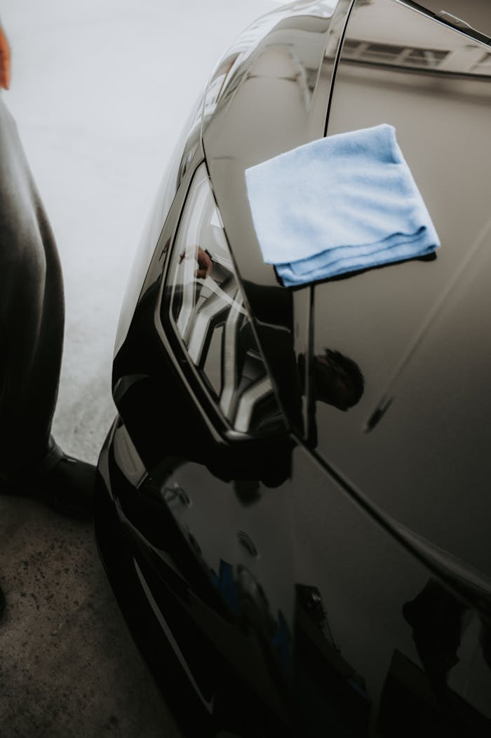 Close-up of a sleek black sports car with polished finish and cloth on headlight.
