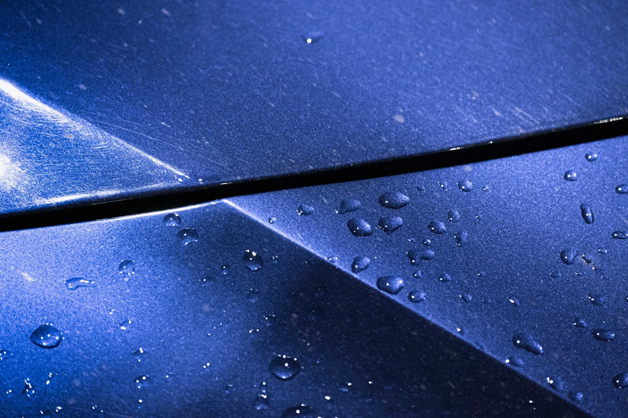 services-01 Detailed shot of water droplets on a shiny blue metallic surface, highlighting texture.