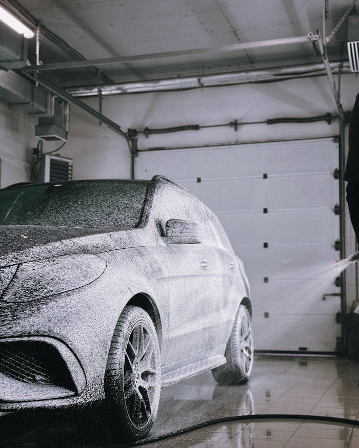 services-04 A luxury car gets foam washed in a modern garage with overhead lighting.
