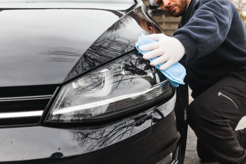 pexels photo 6459729 Close-up of a man cleaning a car headlight using a blue cloth outdoors.